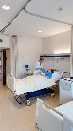 Eine Krankenschwester sieht nach einer Patientin in einem Patientenzimmer des UMCG mit energiesparender Beleuchtung von Philips
