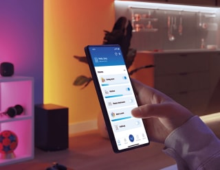 „Eine Frau steuert die smarte LED Beleuchtung über eine Smartphone-App und passt das rosafarbene Umgebungslicht an für ein personalisiertes stimmungsvolles Licht Zuhause."