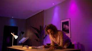 Eine Person sitzt zu Hause über einen Schreibtisch gebeugt, in einem Raum mit buntem Umgebungslicht